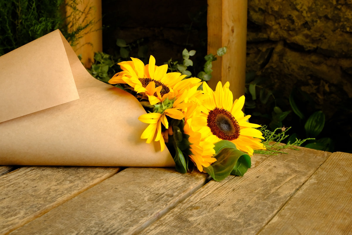 Sunflowers wrapped in brown paper on wooden surface