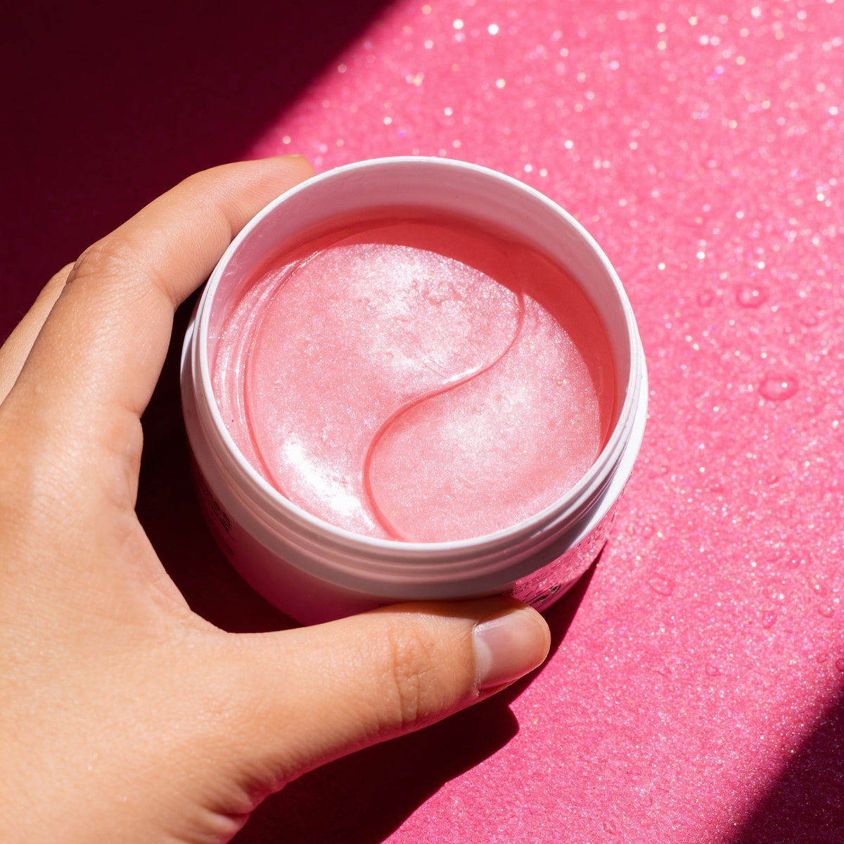 Hand holding an open jar of pink eye masks