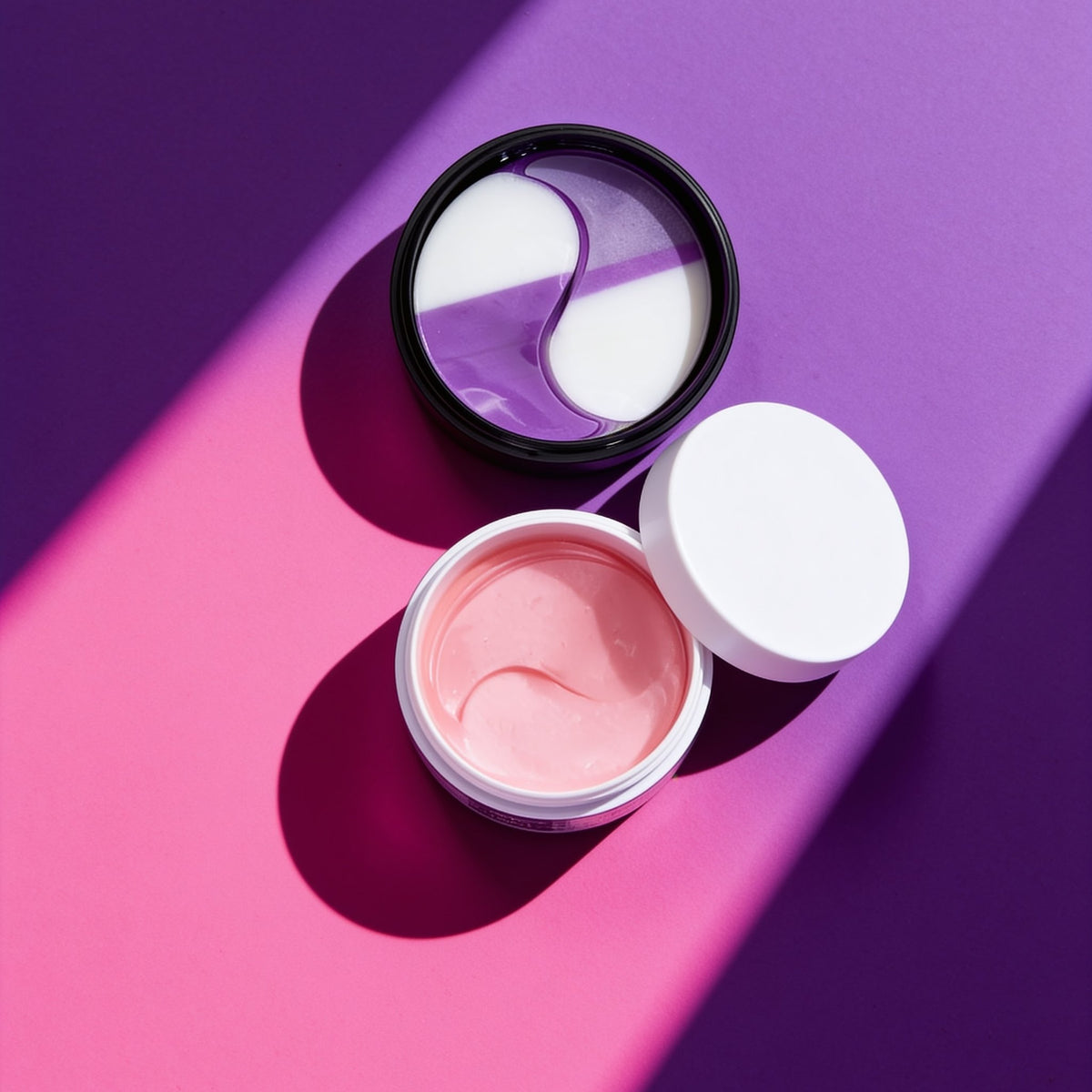 AM + PM Eye Ritual: the white Brightening & Depuffing jar with pink masks and the black Collagen Boost jar with lilac masks, open