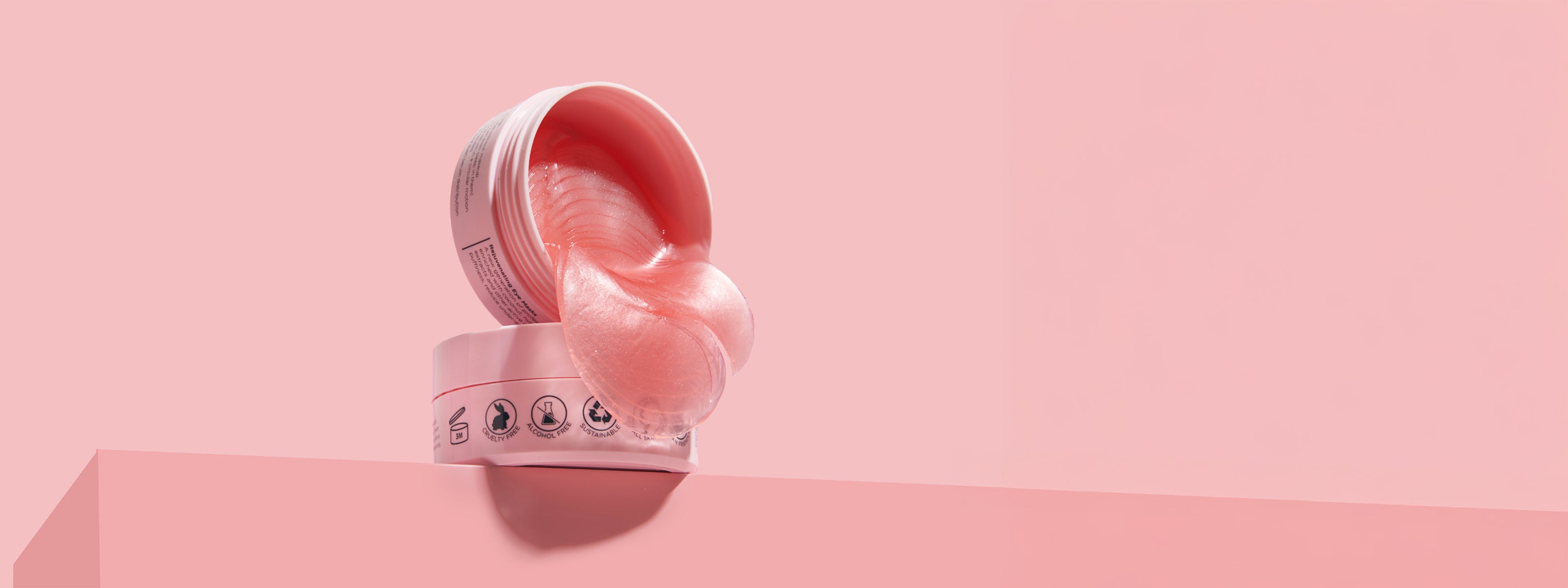Open jar of kenzina eye masks on a pink platform with a pink background